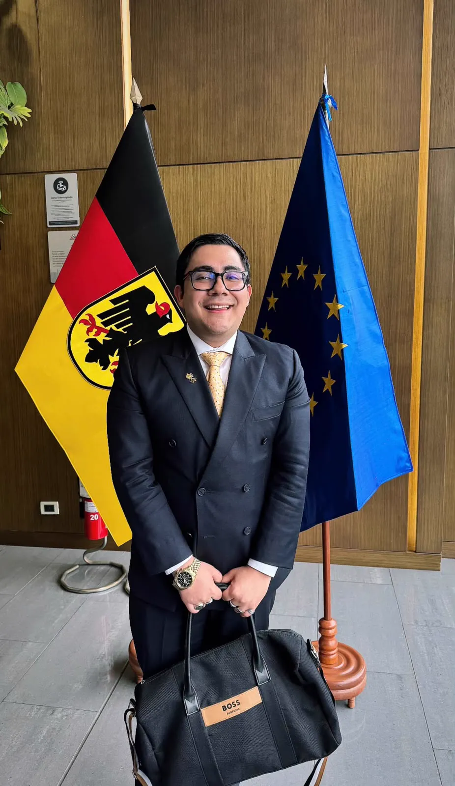 A man in a suit beside the flags of Germany and the European Union