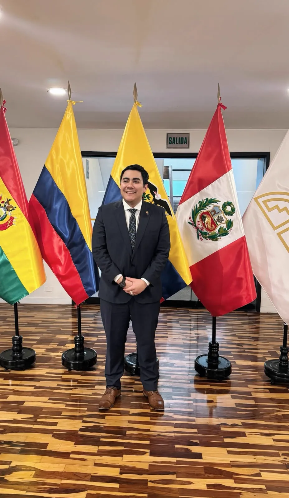 A man in a suit before the flags of Bolivia, Colombia, Ecuador and Peru
